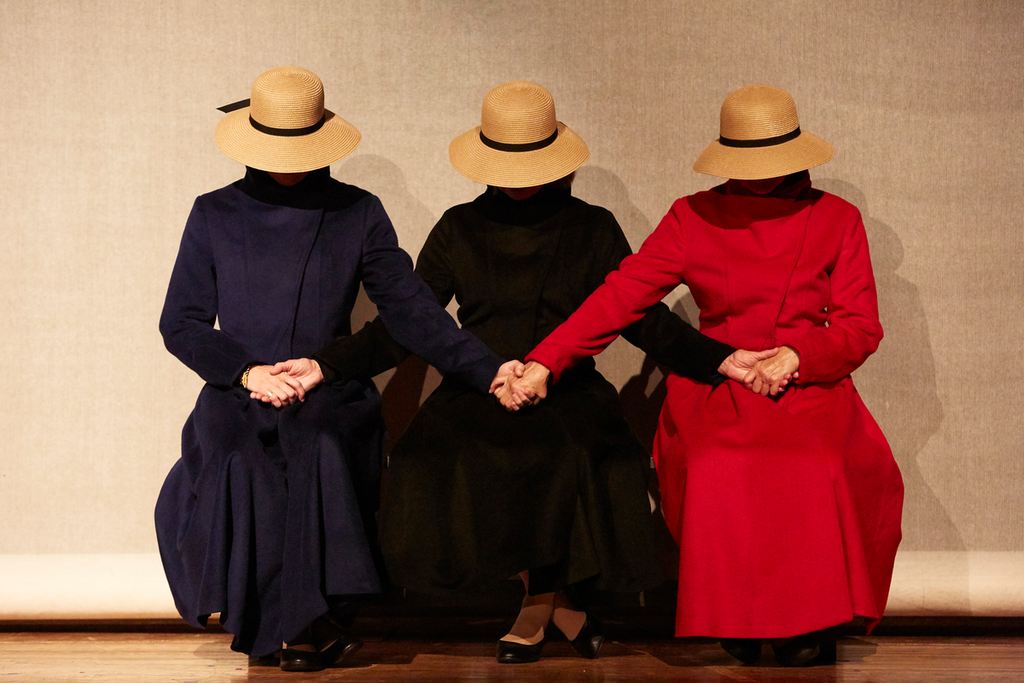 Adult woman reading from a book, audience members are seen in the foreground